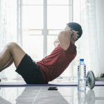 Male fitness instructor showing exercises training at home using laptop.