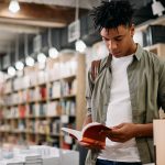 Young black student reading a book in a library,